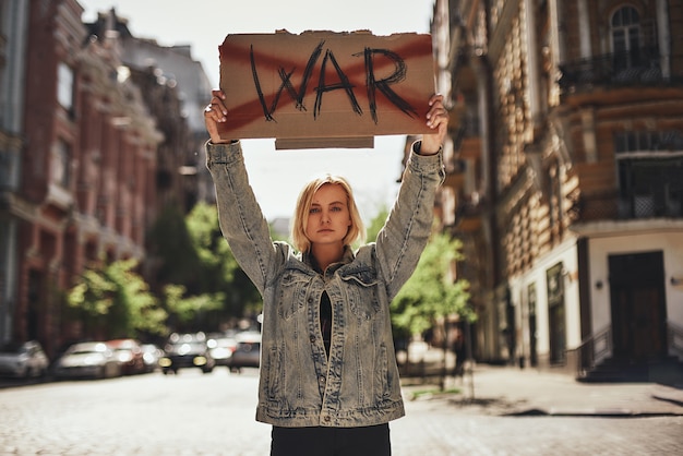 Foto pare a guerra, jovem mulher confiante segurando uma tabuleta com tachado de guerra de palavras enquanto está de pé