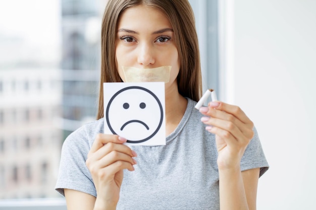 Pare de fumar, mulher segurando um cigarro quebrado e um sorriso triste.