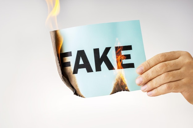 Pare o conceito falso A mão masculina queima o papel com a palavra falsa