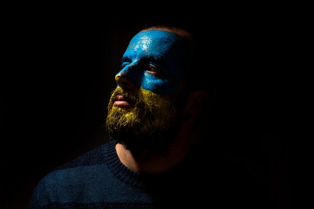 Pare o conflito de guerra entre a Ucrânia e a Rússia Retrato de um jovem com o rosto pintado nas cores azul e amarela da bandeira olhando para a esquerda