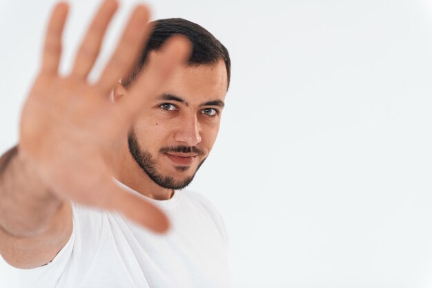 Pare o gesto jovem bonito em pé dentro de casa contra o fundo branco