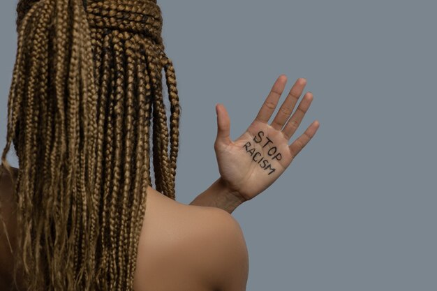 Pare o racismo. Jovem afro-americana de costas com as costas, mostrando a palma da mão com a inscrição "pare o racismo" acima do ombro