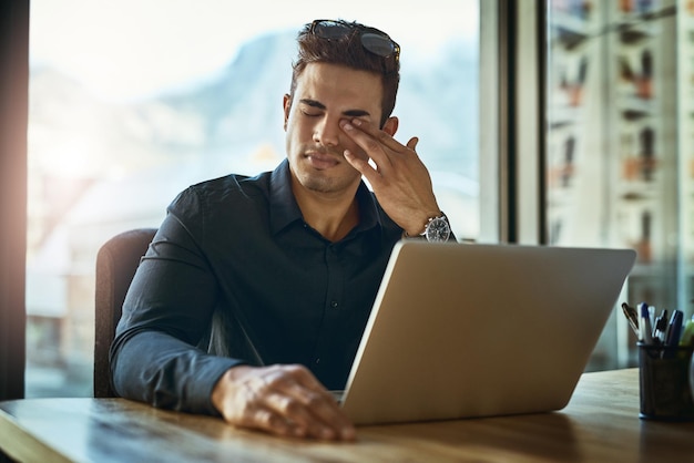 Parece que este día nunca va a terminar Foto de un joven hombre de negocios que parece estresado mientras trabaja en una computadora portátil en una oficina