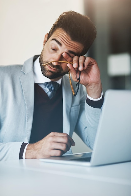 Parece que ya ha perdido su energía y motivación Fotografía de un joven hombre de negocios que parece exhausto mientras trabaja en una computadora portátil en una oficina