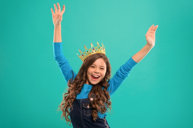 Parece rainha. Garoto usa o símbolo da coroa de ouro da princesa. Senhora pequena princesa. Bebê fofo menina usar coroa enquanto ficar fundo azul. Conceito de infância. Toda garota sonhando em se tornar princesa.