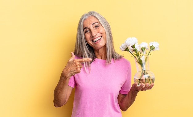 Parecendo animado e surpreso, apontando para o lado e para cima para copiar o espaço segurando flores decorativas