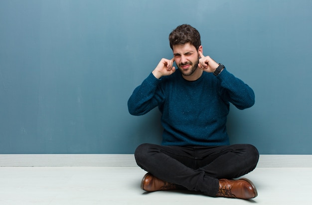 parecendo irritado, estressado e irritado, cobrindo ambos os ouvidos com um ruído ensurdecedor, som ou música alta