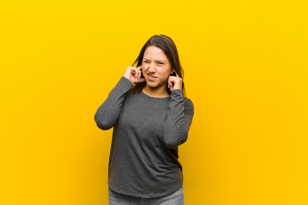 parecendo irritado, estressado e irritado, cobrindo os dois ouvidos com um barulho ensurdecedor, som ou música alta