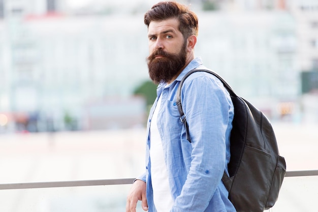 Parecendo mais brutal. Homem caucasiano brutal com barba comprida em meio urbano. Hipster brutal usando mochila em estilo casual. Homem barbudo com aparência brutal ao ar livre.