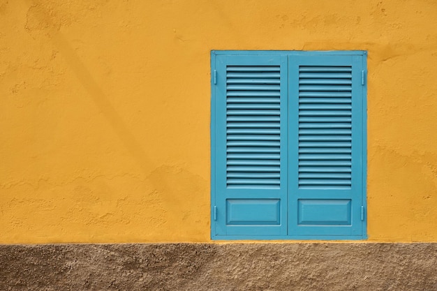 Una pared amarilla pintada con una ventana azul