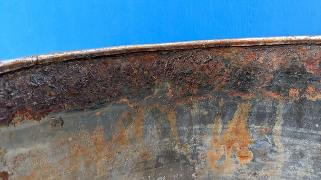 Una pared azul detrás de un contenedor de metal con borde oxidado.