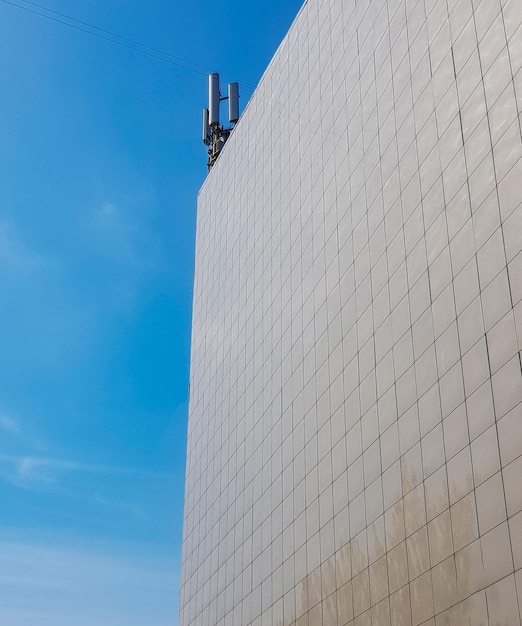 La pared exterior de un edificio moderno de estilo comercial con paneles de tejas en el techo antenas modernas contra el cielo azul