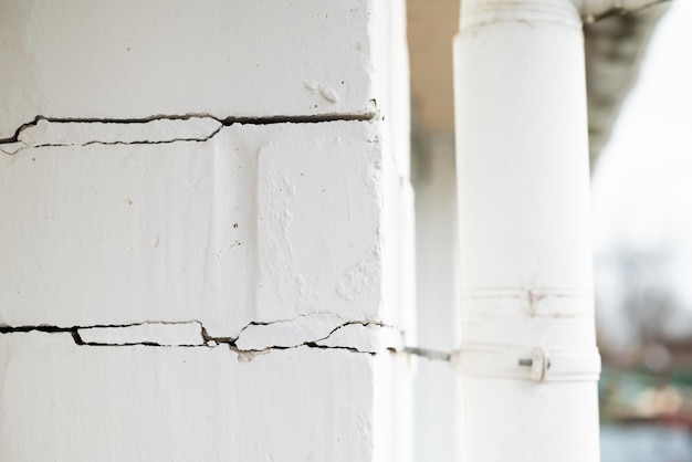 Pared de ladrillo blanco con grietas Casa construida con errores en las paredes de cimientos con grietas