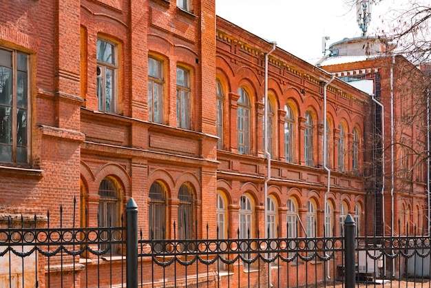 Pared de ladrillo rojo anaranjado de un edificio antiguo con enormes ventanas de arco y valla de hierro negro alrededor Diseño exterior Estilo victoriano Arquitectura Historia Patrimonio histórico Fábrica Industrial