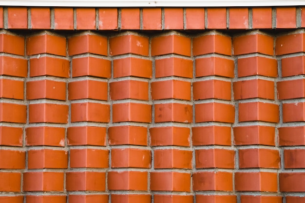 Pared de ladrillo rojo de ladrillos angulares en diagonal. Imagen de fondo geométrica de ladrillos de cuerno marrón. Compuesto con ladrillo liso en la parte superior debajo de la cornisa blanca.