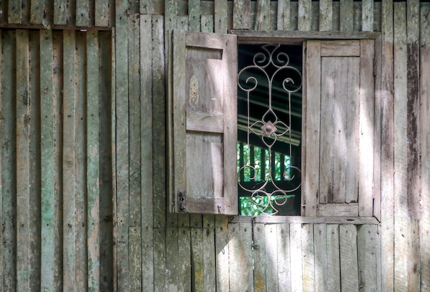 Pared de madera vieja con ventana antigua y acero curvado.