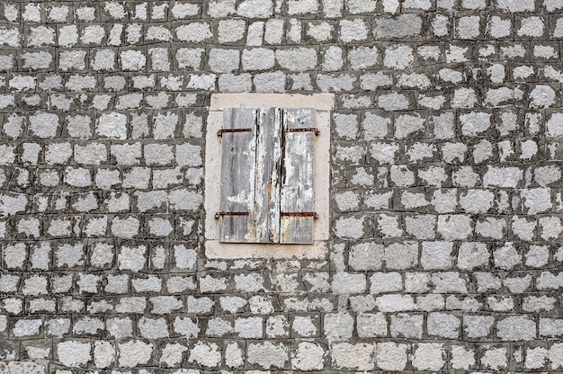 La pared de piedra de la casa vieja, con contraventanas agrietadas en madera clara