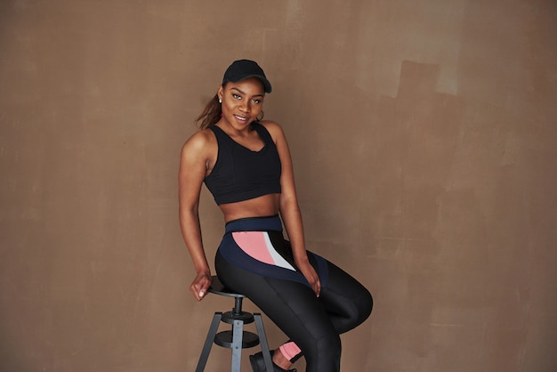 Foto pared pintada de marrón detrás. joven hermosa mujer afroamericana sentada en la silla en el estudio