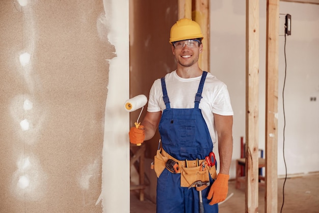 Pared de pintura de constructor masculino alegre en casa en construcción