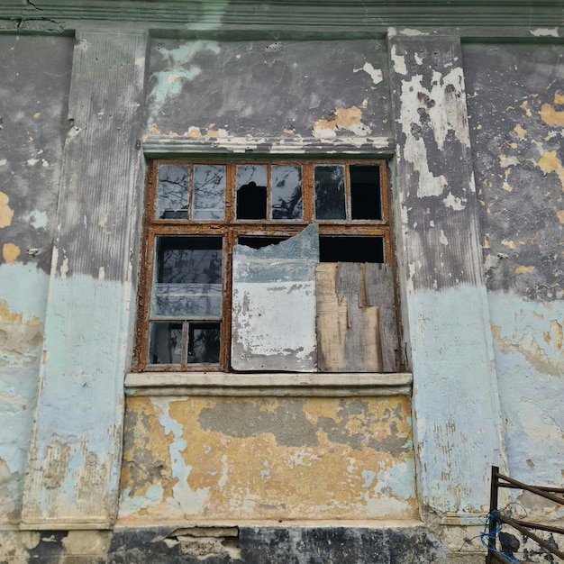 Una pared con una ventana rota que tiene mucha pintura.