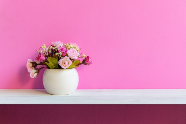 Parede cor-de-rosa com a flor na madeira branca da prateleira, copie o espaço para o texto. Ainda vida conceito