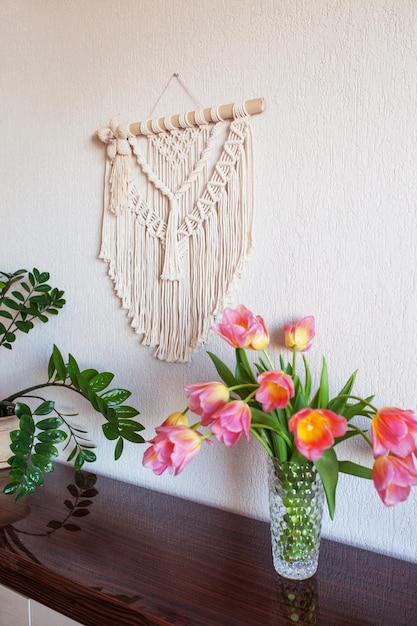 Parede de macramê elegante pendurada na parede branca acima da cômoda Interior aconchegante da sala de estar com flores em macramê de vaso e planta verde pendurada Conceito minimalista de decoração para casa