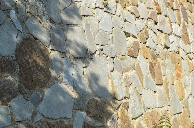 Parede de pedra autêntica, cerca de pedra e cimento, dia ensolarado de verão e sombras na parede.