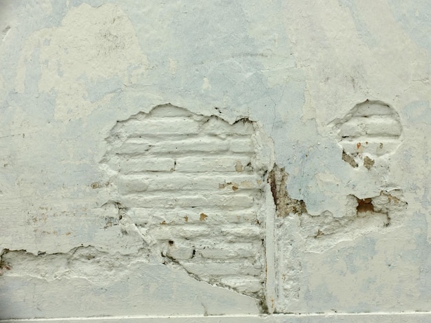 las paredes de la casa están encaladas con cemento desconchado dejando ver los ladrillos. pared de la casa antigua