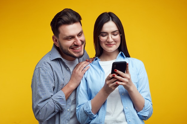 Foto la pareja se abrazan mira con alegría el teléfono móvil