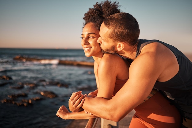 Pareja abrazándose y besándose en la playa con puesta de sol al aire libre con amor y cuidado en el ejercicio de la naturaleza con maqueta de vista al mar Mujer negra hombre y compromiso de relación fitness juntos y gente contenta feliz