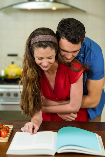 Pareja abrazándose en la cocina mientras revisa el libro de recetas