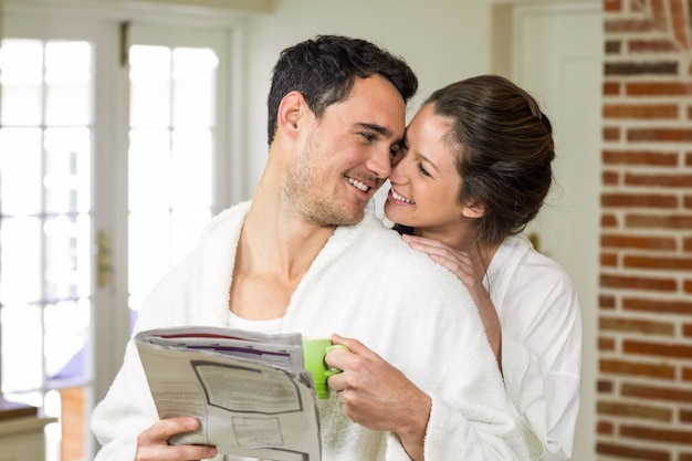 Pareja abrazándose mientras toma un té y leyendo el periódico en la cocina