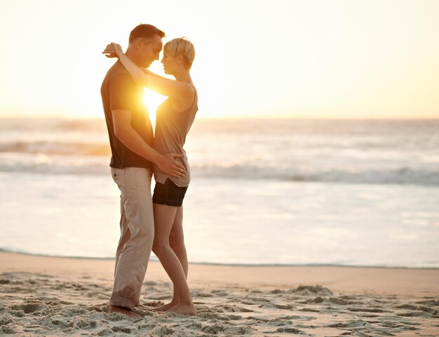 Foto pareja abrazar y romance en el mar al atardecer para relajarse vacaciones y feliz en el viaje compañeros juntos y agua en la playa para disfrutar de la calma y sonreír por el amor del matrimonio en luna de miel y vacaciones