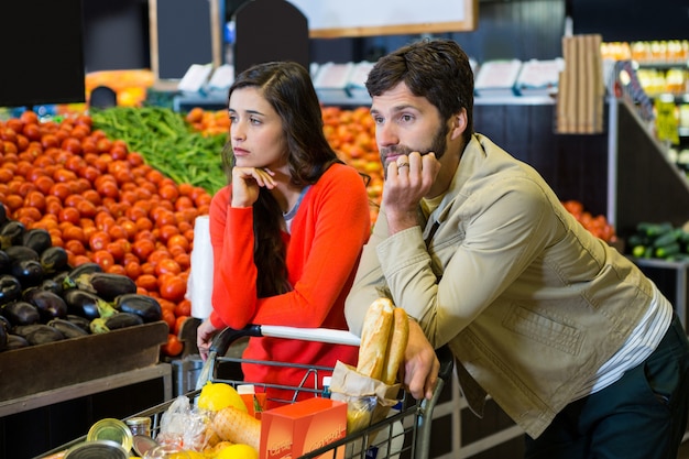 Foto pareja aburrida con carrito de compras en la sección orgánica