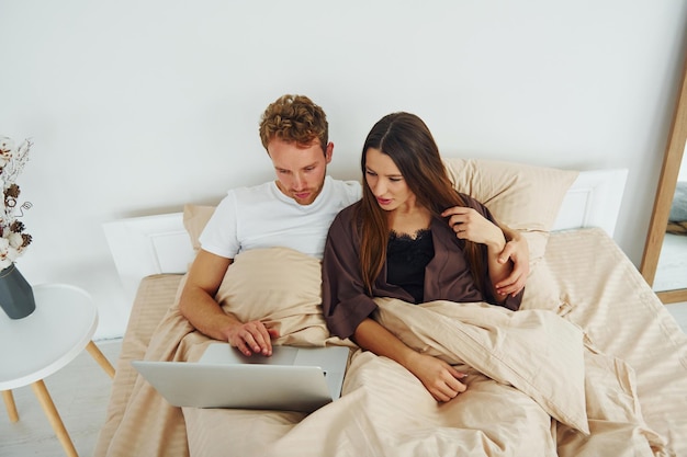 Pareja acostada en la cama con laptop Interior y diseño de hermoso dormitorio moderno durante el día