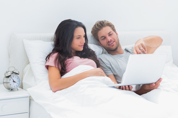 Pareja acostada en la cama mirando una computadora portátil