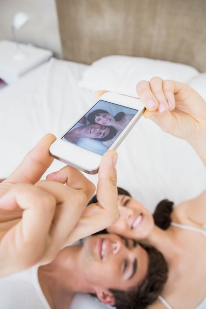 Pareja acostada en la cama y tomando una selfie en teléfono móvil