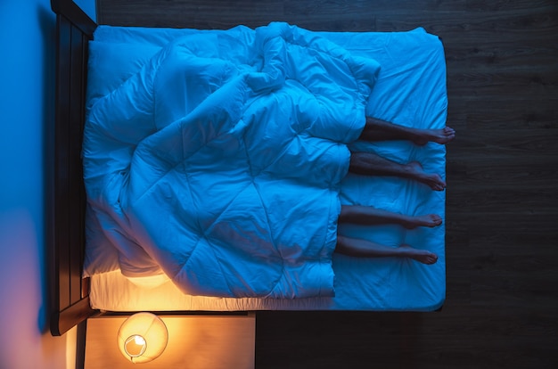 La pareja acostada debajo de un edredón en la cama. tarde, noche, vista desde arriba