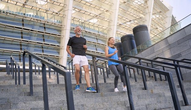 Pareja activa alegre hombre y mujer en ropa deportiva con entrenamiento juntos al aire libre trotar hacia abajo