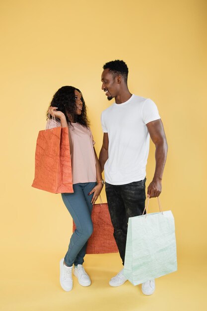 Pareja de adictos a las compras hombre y mujer afroamericanos sosteniendo bolsas de compras