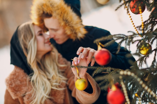 Pareja adulta joven decora el árbol de Navidad en el bosque de invierno. Concepto de celebración de fiesta de año nuevo pino.