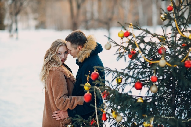 Pareja adulta joven decora el árbol de navidad en el bosque de invierno Concepto de celebración de fiesta navideña de pino de año nuevo