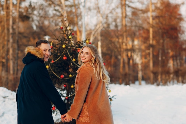 Pareja adulta joven decora el árbol de navidad en el bosque de invierno Concepto de celebración de fiesta navideña de pino de año nuevo