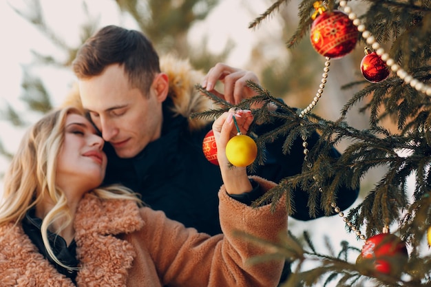 Pareja adulta joven decora el árbol de navidad en el bosque de invierno Concepto de celebración de fiesta navideña de pino de año nuevo