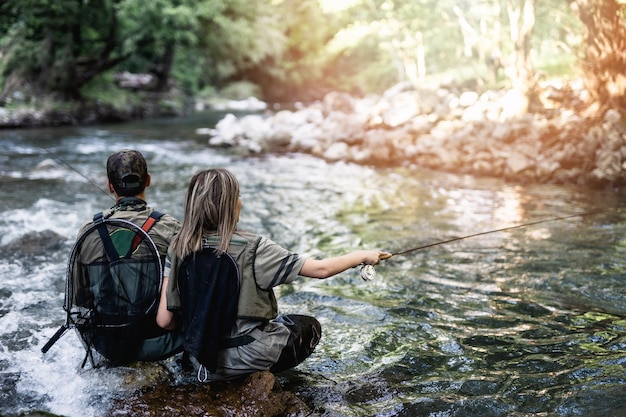 Foto la pareja adulta joven está pescando juntos en el río rápido de la montaña. gente activa y concepto de pesca con mosca deportiva.