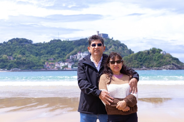 Pareja adulta latina en la playa sonriendo mirando a la cámara y en primavera