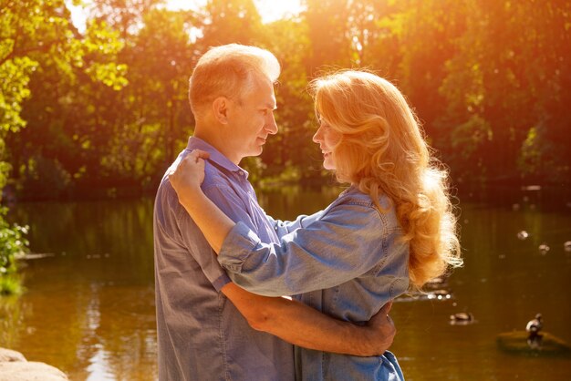 Una pareja adulta se para a la orilla del lago en un abrazo bajo los rayos del sol poniente