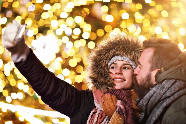 Pareja adulta tomando selfie en la ciudad durante la época navideña