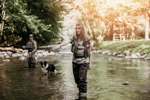 Una pareja de adultos jóvenes con perro está pescando juntos en un rápido río de montaña. Gente activa y concepto de pesca con mosca deportiva.