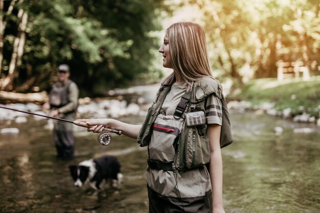 Pareja de adultos jóvenes con perro está pescando juntos en el río rápido de la montaña. Gente activa y concepto de pesca con mosca deportiva.